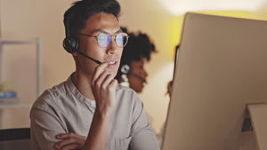 Remote digital support consultants with headset and glasses looking at monitor and talking.