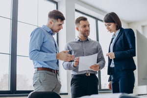 Three people in an office looking at a paper and talking to each other.