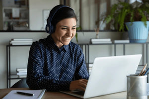 Remote online consultant woman with headphones smiling at monitor with notebook and pen next to her.