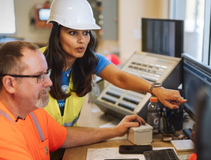Samsara consultant wearing a hardhat and reflective vest pointing to monitor and helping client at a jobsite.