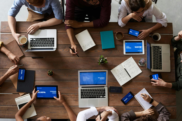 Team sitting in circle around table having a discussion with laptops and notebooks.